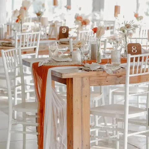 Reception table with burnt-orange runner, glassware and dried floral accents