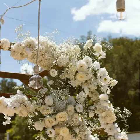 Floral arch dressed with white roses and baby's breath, festoon bulbs hanging above