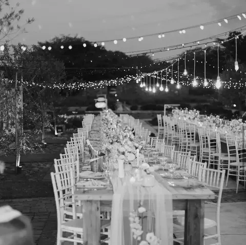 Long reception table at dusk under festoon lights, shown in black and white