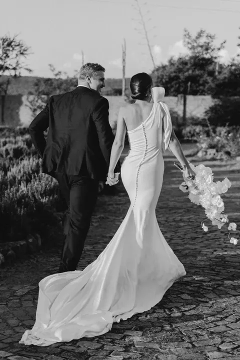 Black-and-white photo of a couple walking hand in hand with a cascading white bouquet