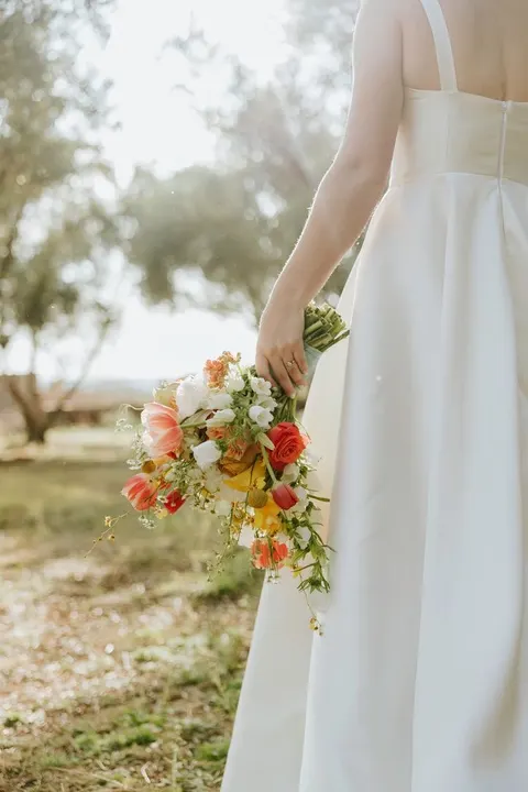 Bride holding a loose coral and yellow wildflower bouquet