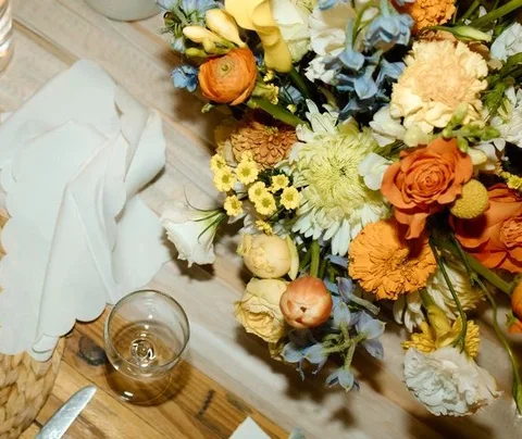 Orange, yellow and blue centerpiece beside a folded napkin and wine glass