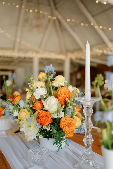 Orange, yellow and blue centerpiece under string lights in a barn