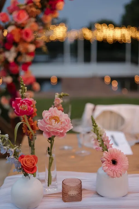 Bud vases of pink, coral and orange blooms on a dusk-lit table