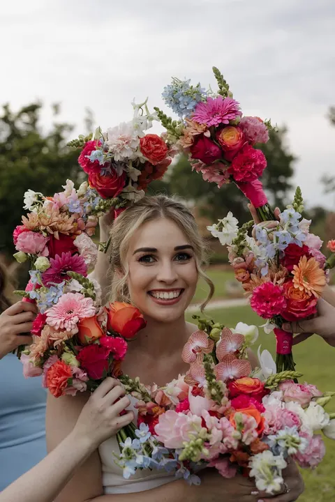 Bride encircled by vivid pink, coral and blue bridesmaid bouquets