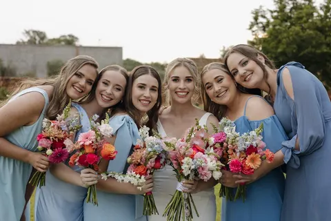 Bride and bridesmaids in dusty blue holding vivid pink and coral bouquets