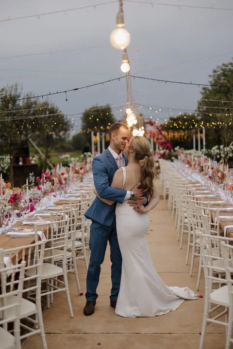 Couple embracing between reception tables dressed in pink and coral at dusk