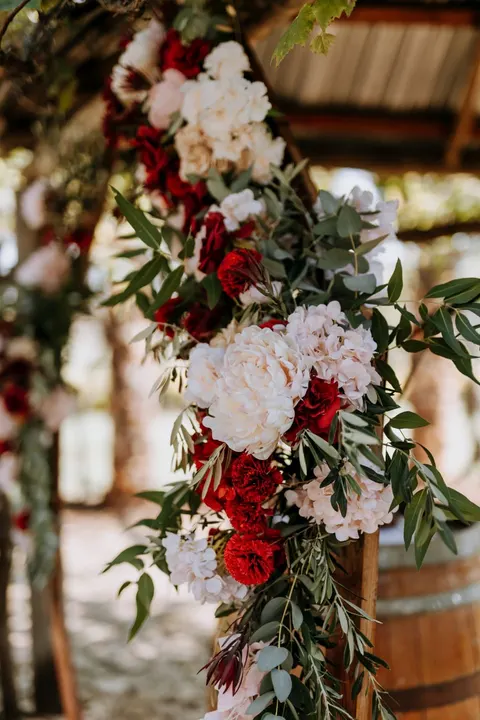 Deep red and white floral garland dressing a wooden ceremony arch