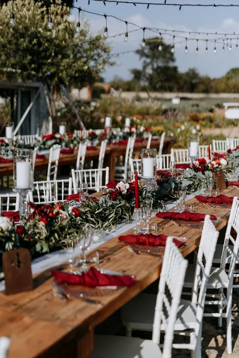 Long reception table dressed in red garlands under string lights