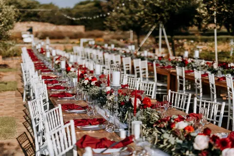 Wide view of long reception tables dressed in red florals under string lights