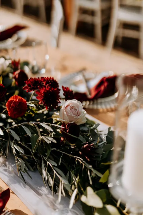 Table garland detail with a blush rose among red dahlias and white peonies