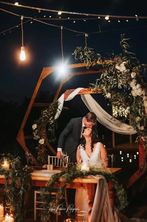 Couple sharing a kiss beneath a white floral hexagon arch at night