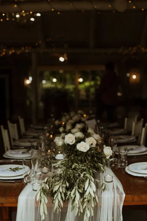 Indoor evening reception table dressed with cream roses and olive garland