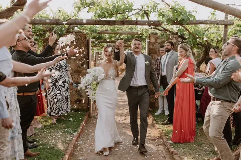 Newlyweds walking through a confetti toss beneath a grapevine pergola